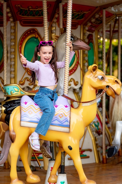 Una niña en un parque de diversiones monta en un carrusel y sonríe con felicidad mostrando a la clase el concepto de fines de semana y vacaciones escolares