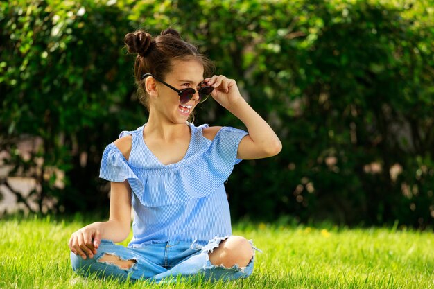 Una niña en el parque con ropa azul sentada en el césped. un niño con gafas de sol. Foto de alta calidad