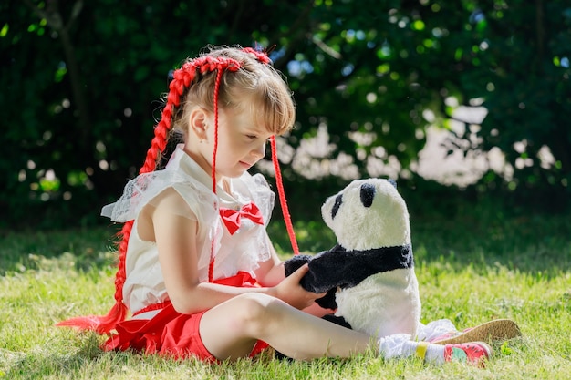 Una niña en el parque en verano sentada con un panda de juguete. Foto de alta calidad