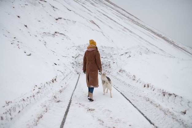 Una niña pasea a su perro por el bosque de invierno.