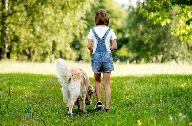 Niña paseando a un perro en la pradera