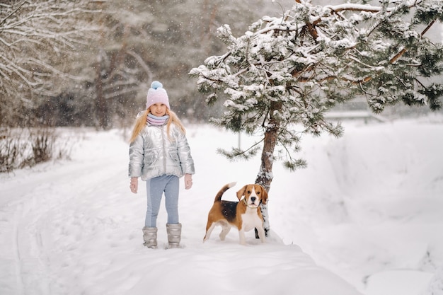 Una niña en un paseo con su perro en el bosque de invierno. el dueño y el perro están jugando en el bosque nevado