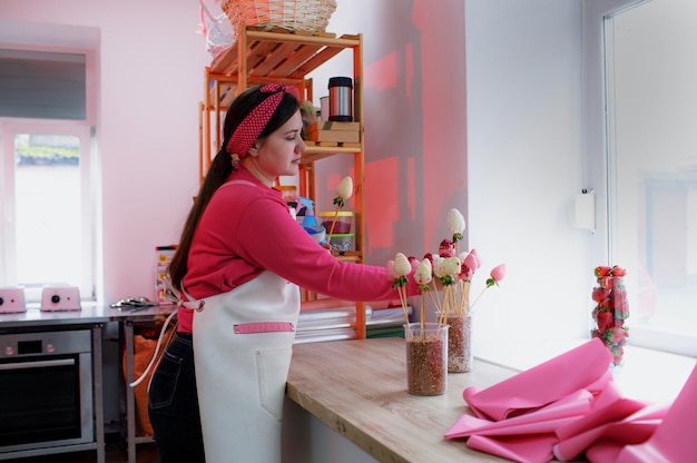 Una niña pastelera con un delantal blanco prepara fresas en chocolate multicolor, deliciosos postres de fresa. Ramo de fresas.