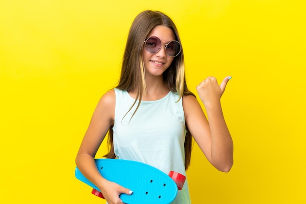 Niña patinadora caucásica aislada de fondo amarillo con un patín y apuntando hacia un lado