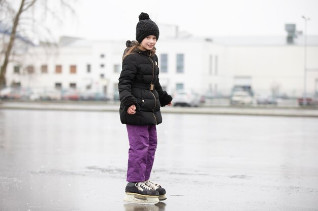 La niña va a patinar sobre hielo en el invierno con el telón de fondo de la ciudad.