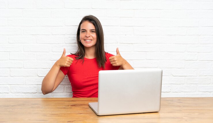 Foto niña con pc en una mesa dando un gesto de pulgares arriba