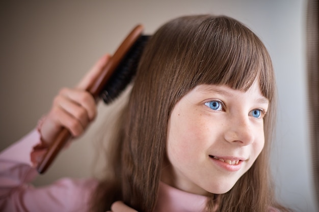 Niña con pecas y ojos azules peinándose el pelo.