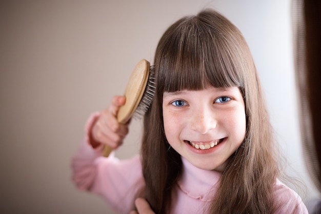 Niña con pecas y ojos azules peinándose el pelo.