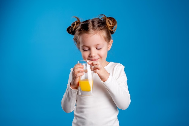 Niña con un peinado divertido en una camiseta blanca sostiene un vaso con jugo en sus manos azul