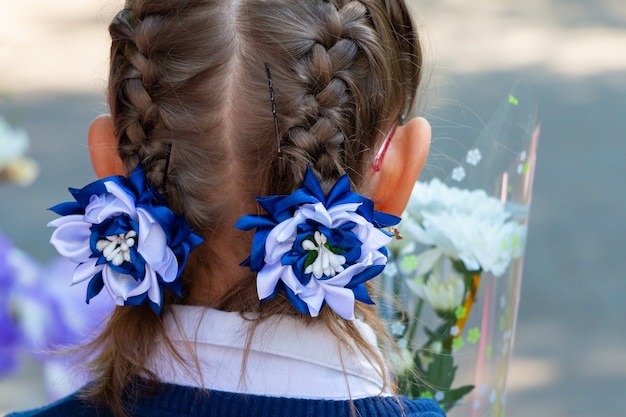 Niña con un peinado de moda para las fiestas. Chica con coletas y flores decorativas tejidas en ellos