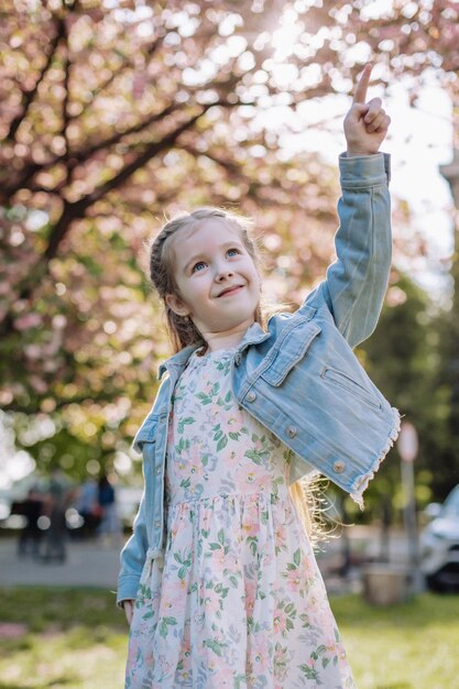 La niña pelirroja apunta cuesta arriba sobre un fondo de sakura en el jardín