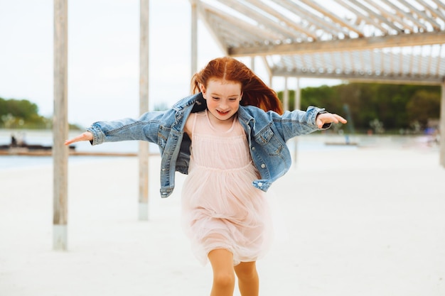 Niña pelirroja corre sobre la arena en la ciudad niño feliz nadando en la playa