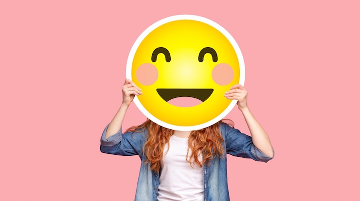 Foto niña pelirroja escondiendo su cara detrás de una sonrisa emoji feliz