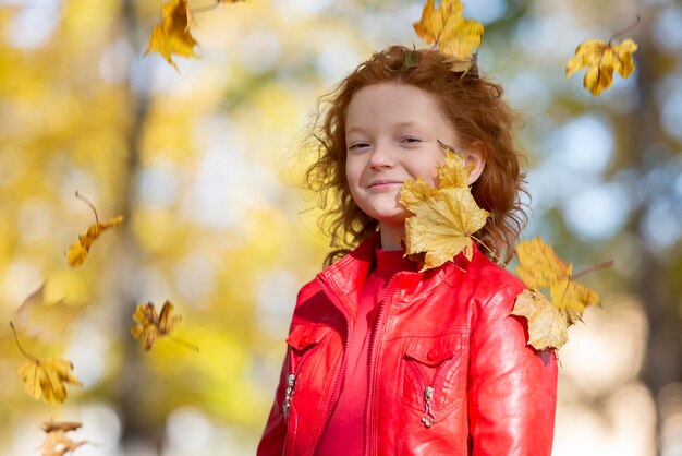 Niña pelirroja feliz ríe y juega con hojas de otoño