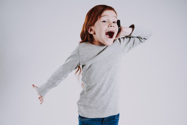 La niña pelirroja habla en el teléfono con admiración.