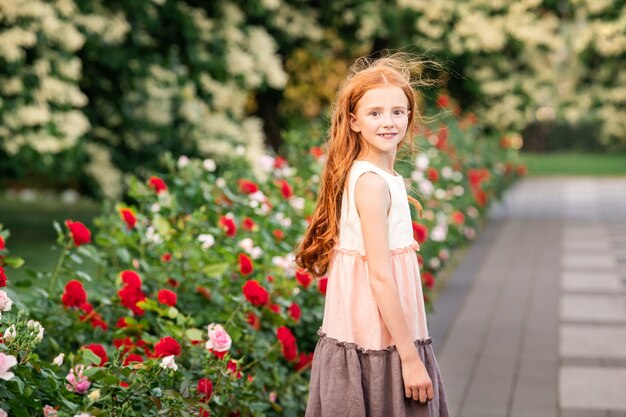 Niña pelirroja oliendo una rosa en el jardín floreciente en verano