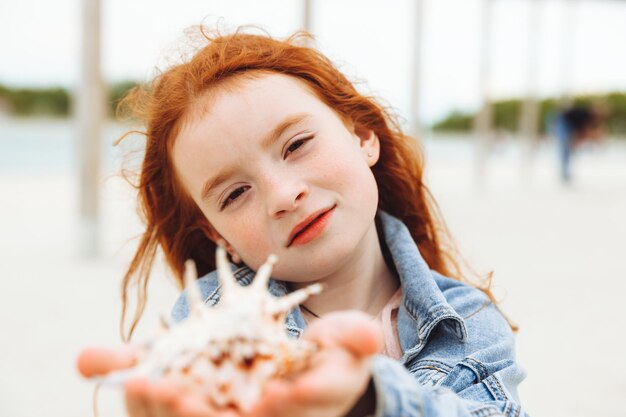 Una niña pelirroja sostenía una concha en la oreja Vacaciones de verano