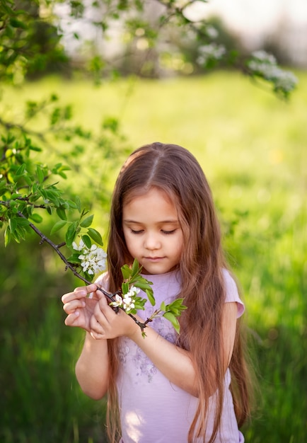 Niña con el pelo largo cerca de un árbol en flor en la naturaleza