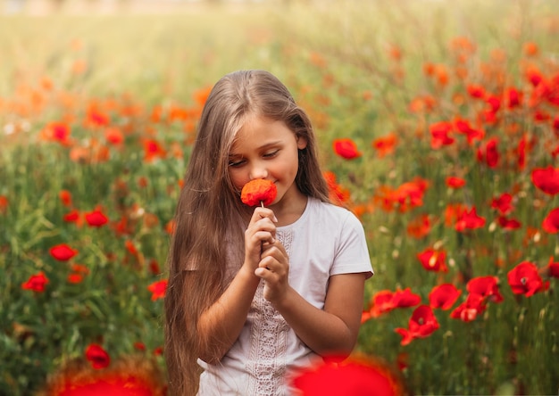 Niña de pelo largo posando en el campo de amapolas con sol de verano