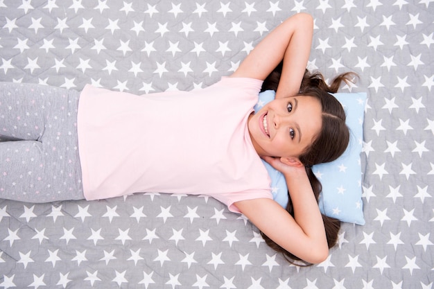 Niña de pelo largo yacía despierta vista superior. La calidad del sueño depende de muchos factores. Chica yacía sobre una almohada pequeña llena de energía en el fondo de la ropa de cama de la mañana. Elija la almohada adecuada para dormir bien.