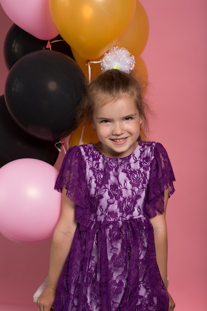 Niña de pelo oscura con globos de colores sobre fondo rosa