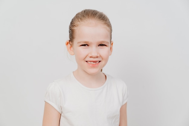 Una niña con el pelo recogido en una camiseta blanca se encuentra sobre un fondo blanco y sonríe