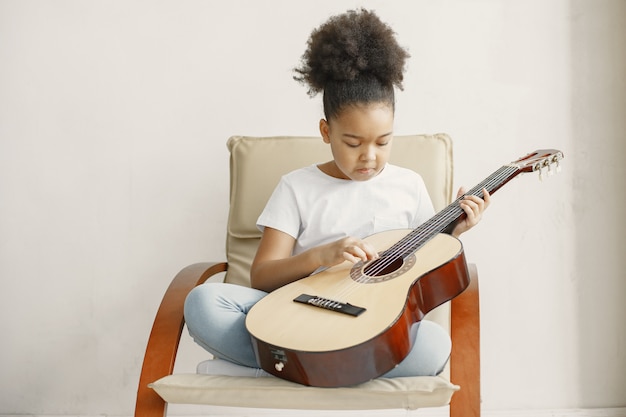 Niña con pelo rizado. Aprendiendo a tocar la guitarra. Niña en una silla.