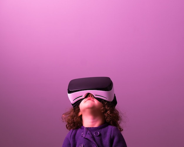 Niña de pelo rizado con gafas de realidad virtual y ropa morada mirando hacia arriba