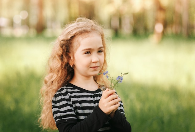 Niña con pelo rizado en el parque con un ramo de flores silvestres