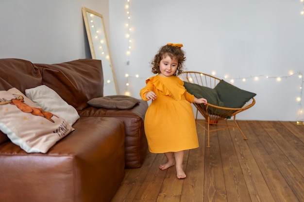 una niña de pelo rizado con un vestido amarillo juega junto al sofá girando