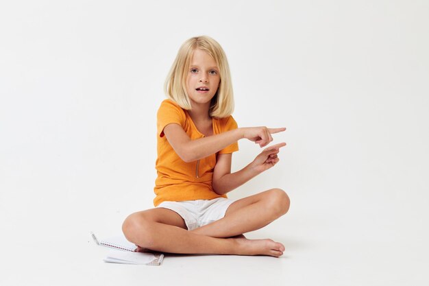 Niña con el pelo rubio gesticulando con las manos mientras se sienta en el suelo