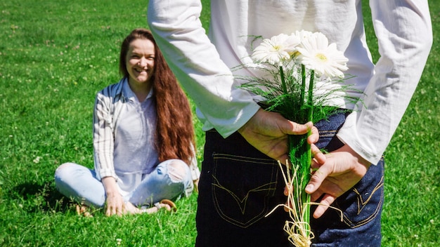 Una niña con el pelo rubio peinado en un moño le da a su madre un ramo de flores blancas