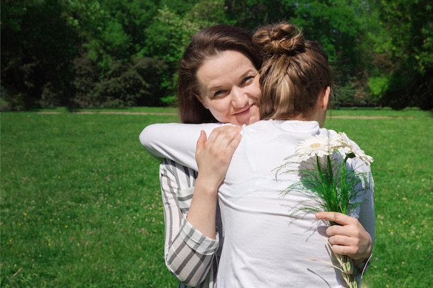 Una niña con el pelo rubio peinado en un moño le da a su madre un ramo de flores blancas