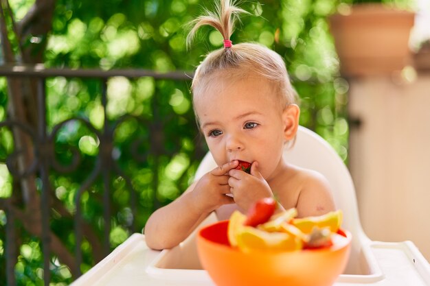 Niña pensativa se sienta en una silla alta y come fresas