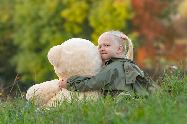 Niña pequeña abraza a un oso de peluche en el parque el día de otoño Vista posterior Niño jugando con un juguete suave afuera