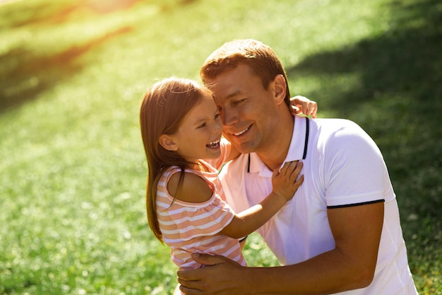 Niña pequeña abrazando a su papá en el parque con fondo borroso