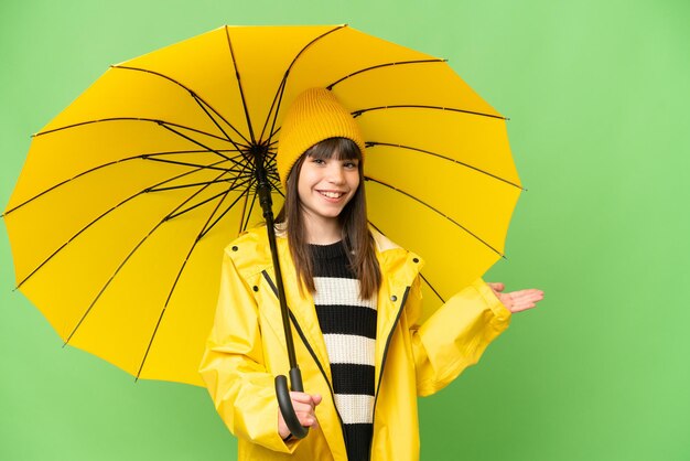 Niña pequeña con abrigo a prueba de lluvia y paraguas sobre un fondo aislado de clave de croma extendiendo las manos a un lado para invitar a venir