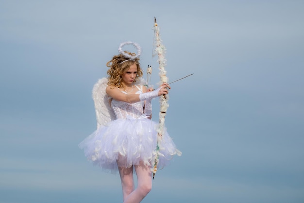 Niña pequeña con alas de ángel y halo Niña pequeña con traje de ángel vestido blanco y alas de plumas Dulce niña ángel Retrato de pequeña niña ángel rubia rizada Concepto de niño inocente