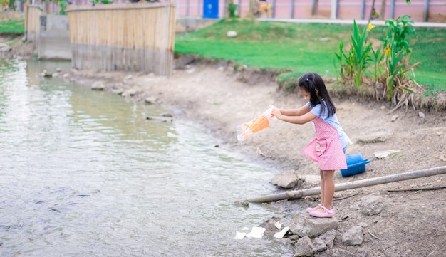 Una niña pequeña alimentación de peces en el estanque en el parque público