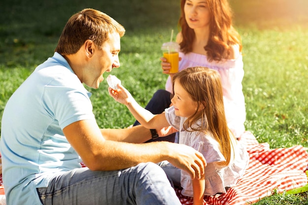 Niña pequeña alimentando a papá con malvavisco en un picnic en el parque