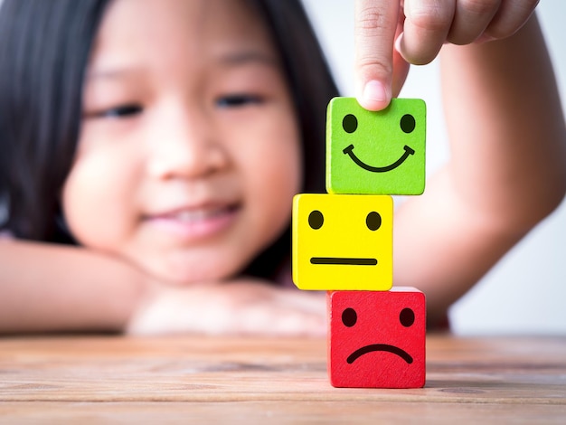 Niña pequeña de Asia poniendo una cara sonriente feliz encima de un icono de cara neutral y triste o infeliz