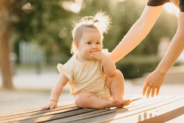 Una niña pequeña en el banco cerca de la mano de una madre en el parque bajo las luces del sol