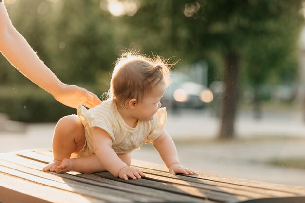 Una niña pequeña en el banco cerca de la mano de una madre en el parque bajo las luces del sol