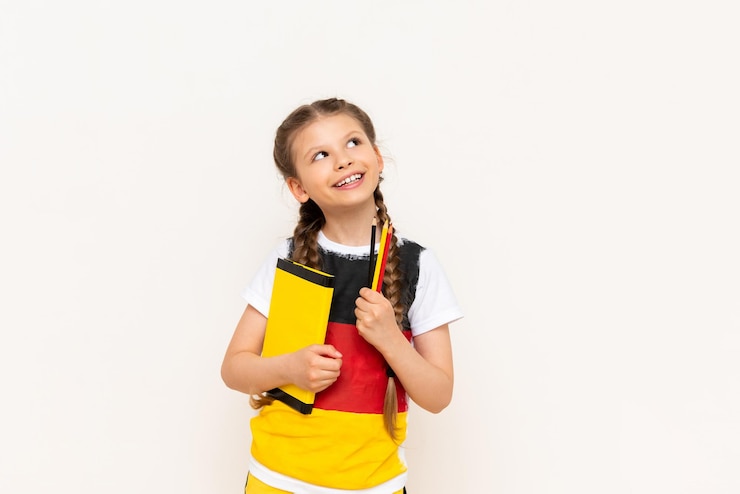 Foto una niña pequeña con una bandera alemana en su camiseta mira cuidadosamente su anuncio en un fondo blanco aislado cursos de alemán para niños