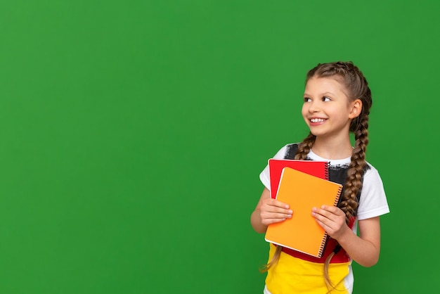 Una niña pequeña con una bandera alemana en su camiseta mira su anuncio en un fondo verde aislado Cursos de alemán para escolares Copiar espacio