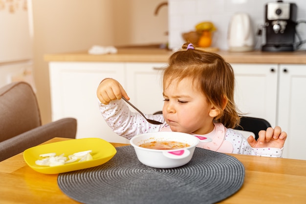 La niña pequeña del bebé come la sopa con la cuchara en su mano.