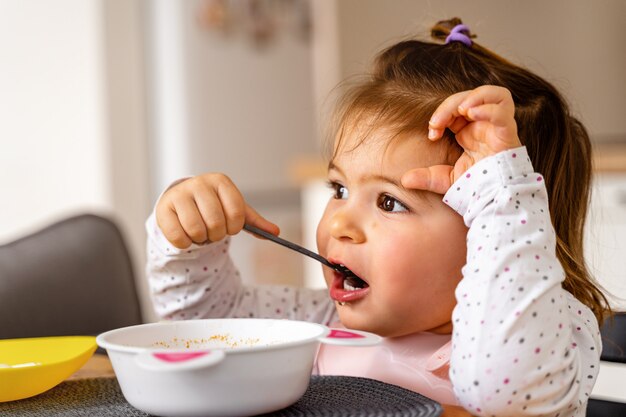 La niña pequeña del bebé come la sopa con la cuchara en su mano.