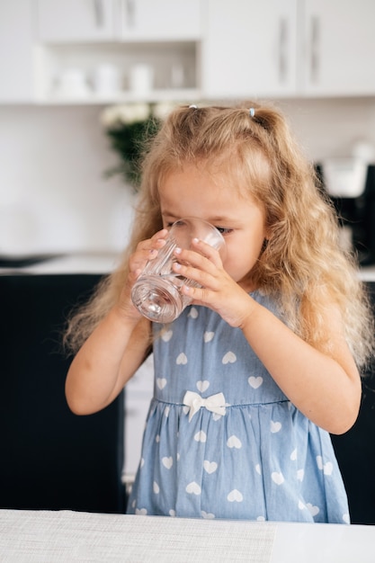 Niña pequeña bebiendo agua en casa del vaso