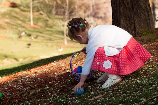 Niña pequeña en búsqueda de huevos de Pascua en parque urbano.