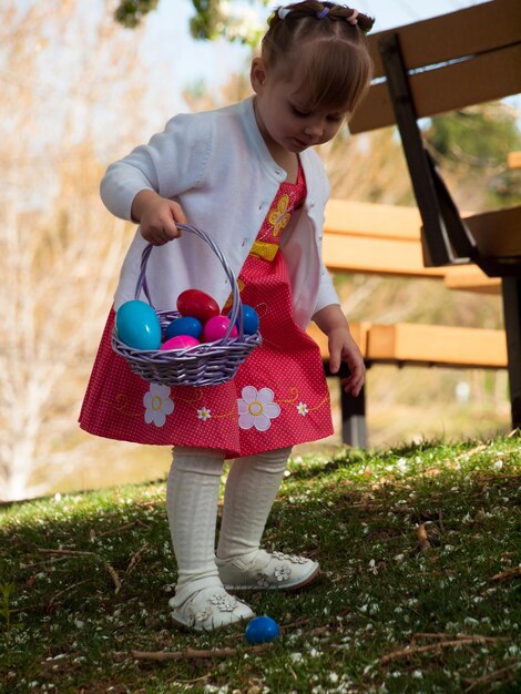 Niña pequeña en búsqueda de huevos de Pascua en parque urbano.